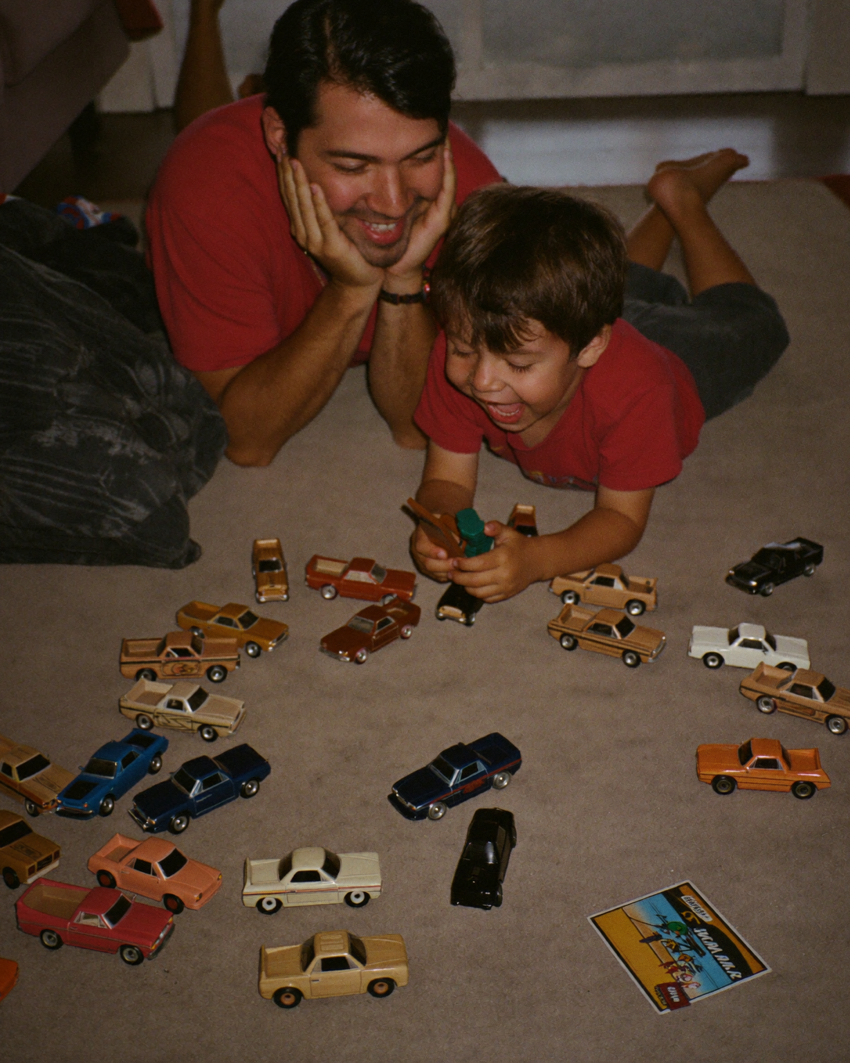 A father and son lying on the floor amid a spread of toy cars