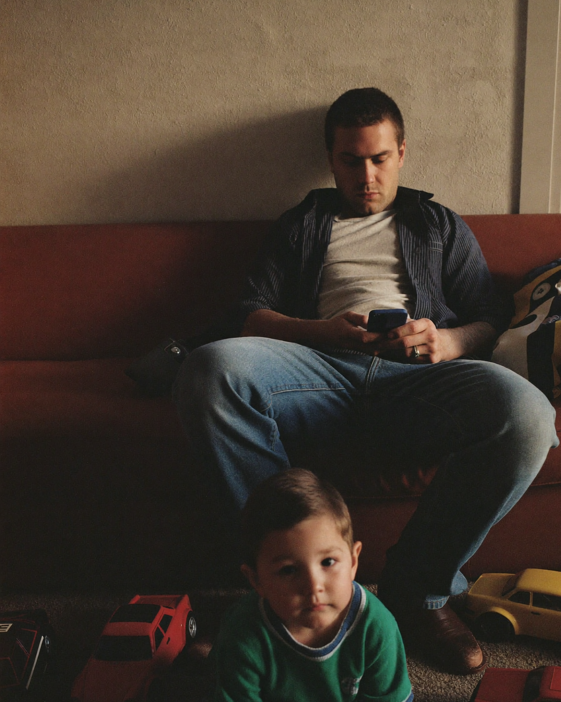 A father absorbed in his phone while his son plays alone below